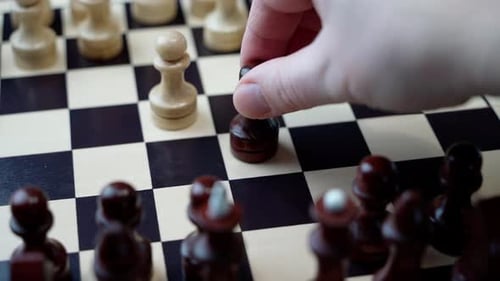 A man's hand makes a move with a black pawn during a game of chess.