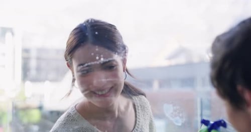Glückliches Paar putzt gemeinsam Fenster, fleißiger Frühjahrsputz mit Lächeln, Sprühflasche und Seife