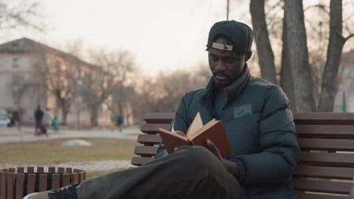 Mann liest Buch auf Parkbank mit verschwommenen vorbeifahrenden Menschen
