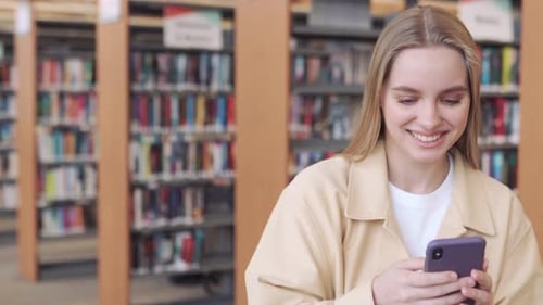 Girl Student Using Phone Looking at Cellphone Standing in University Library