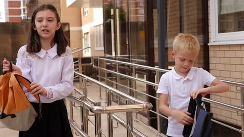 Two Schoolchildren are Talking Outside the School and Putting on Backpacks