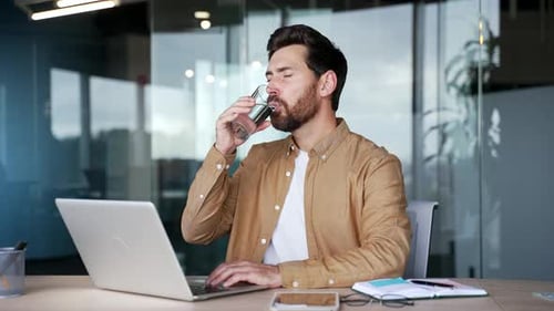 Man Working on Laptop While Drinking Water Indoors