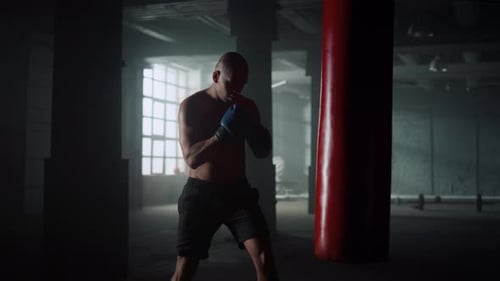 Multiethnic Professional Boxer Silhouette Practicing Kicks On Punching Bag In Dark Gym. Muscular ...