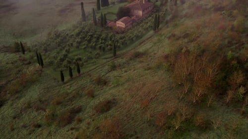 Aerial view of misty countryside with villa and cypress trees, Italy.