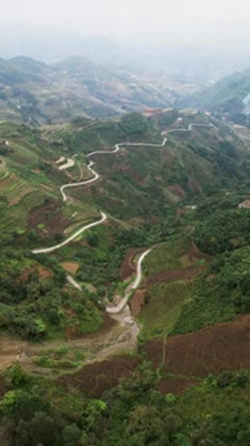 Images aériennes verticales d'une route sinueuse traversant des pentes abruptes en terrasses dans les montagnes du nord du Vietnam
