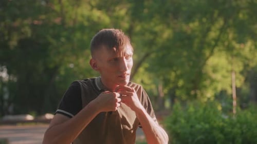 Young Man Buttons Polo Shirt Outdoors in Park