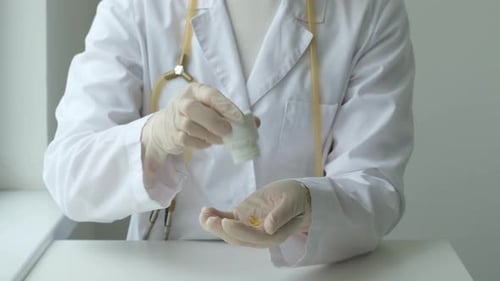 Female Doctor Pours Medicine From a Vial on Hand and Showing Yellow Capsule Pill