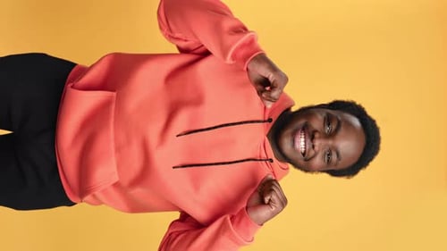 VÍDEO VERTICAL POV Retrato de homem negro muito feliz sorrindo dançando isolado no fundo laranja do estúdio