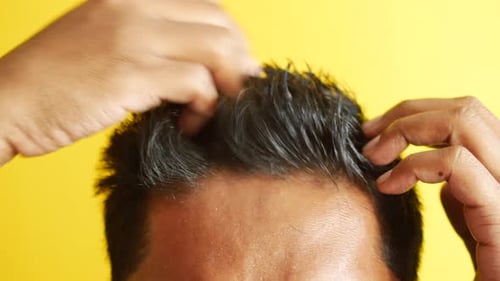 Man Styles Hair Against Yellow Background