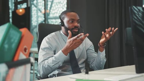 Smiling African American Handsome Man Uses Headphone for Work Speaking on Computer in Modern Office