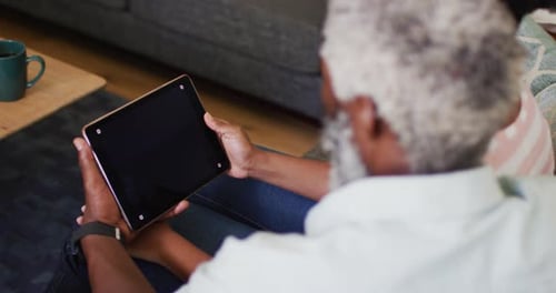 African american senior man sitting on sofa making video call using tablet