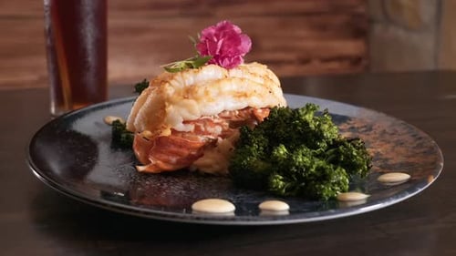 Broiled Maine lobster tail garnished with roasted broccolini and orzo on a black stoneware plate, sl