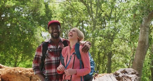 Happy diverse couple with backpacks embracing in park, slow motion