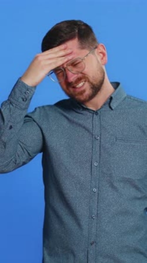 Man in blue shirt touches head in distress