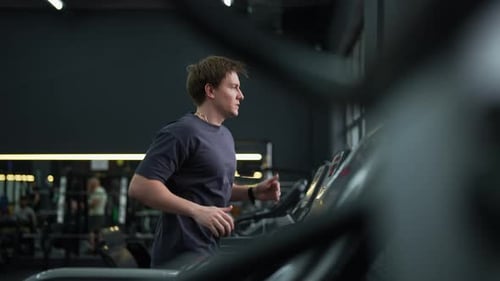 Tracking Shot of Young Athletic Man Jogging on Gym Machine Having Cardio Session in Wellequipped