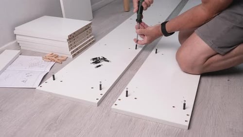 Assembly of cabinet parts at home, a male screws a screw into a furniture board.