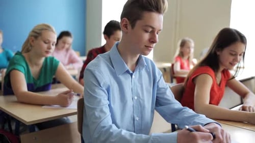 Education, People And Learning Concept - Group Of Students With Notebooks Writing Test At School