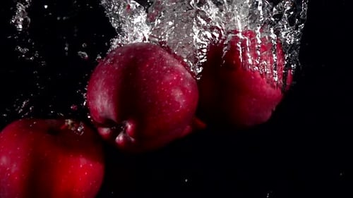Roter Apfel in Zeitlupe, der unter Wasser fällt, auf schwarzem Hintergrund