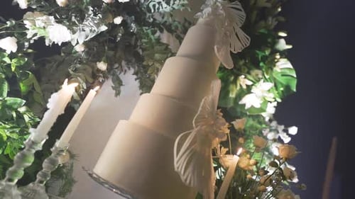 Large white wedding cake in front of green foliage decoration. Crane camera movement