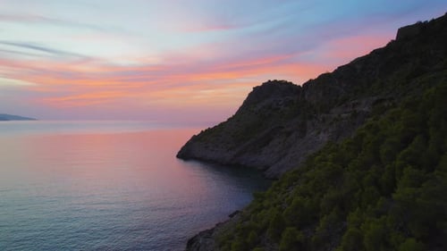 Silhouette de falaise côtière spectaculaire au-dessus d'une mer calme sous un ciel ionien pastel brillant au coucher du soleil