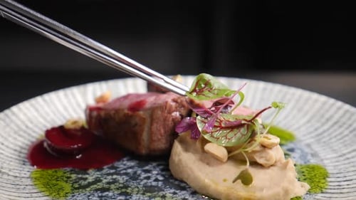 Exquisite Meat Dish Being Plated with Fresh Garnish