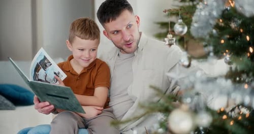 Papá e hijo decoran el árbol de Navidad y revisan un álbum de fotos antiguo