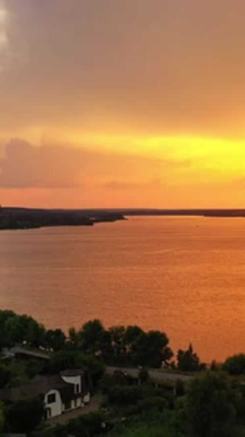 Aerial view of rural place at orange sunset. Golden path of evening sun reflects in the water.