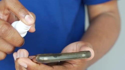 Hands Spraying Disinfectant on Phone Surface