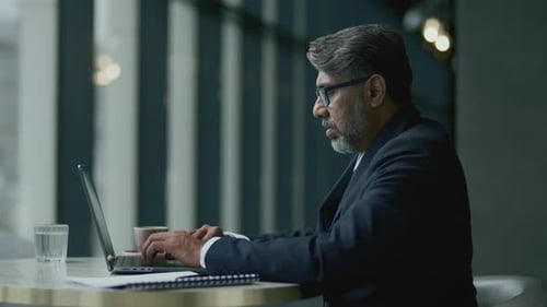 Mature Businessman Drinking Coffee and Typing on Laptop in Restaurant