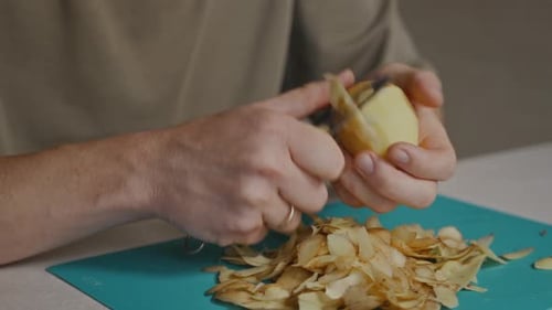 Hände schälen Kartoffel über einem Haufen Gemüseschalen aus nächster Nähe