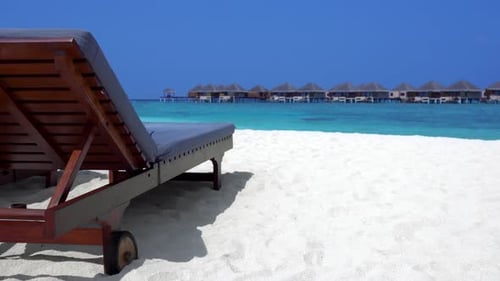 Wooden Sunbeds on Sandy Beach with Water Bungalows in Background