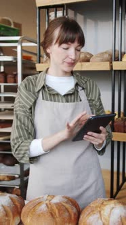 Trabajador de panadería contando barras de pan fresco y usando una tableta digital