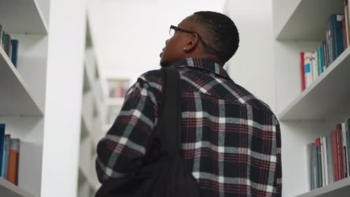 Man Walks Between Bookcases in Library