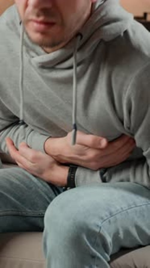 Mann umklammert sich vor Schmerzen an den Magen, Person, die an Verdauungsproblemen leidet
