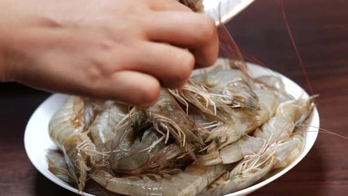 A person places shrimp on a plate and cuts them. Close-up of fresh shrimps in a bowl