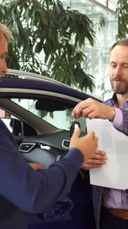 El concesionario de automóviles entrega alegremente las llaves al nuevo propietario encantado
