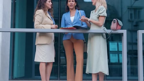 Group of businesswomen standing outside in front of modern office talking.