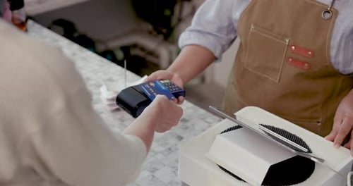 Customer completing contactless credit card transaction while paying to asian senior female cafe