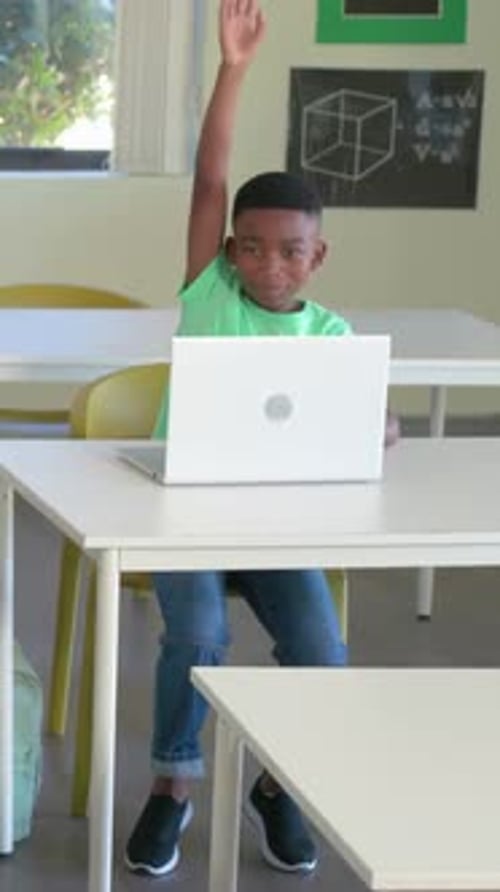 Vertical video: Raising green-tee student after teacher cue in class, leaning to read white laptop