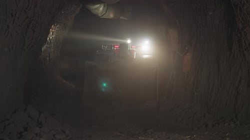 Heavy Mining Vehicle with Big Dipper Drives Into Dark Mine