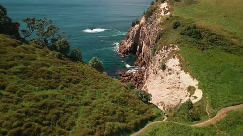Cinematic aerial shot of hiker climbing path along cliff top mountain edge