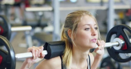 Young beautiful girl in the gym doing exercises on the squat with a barbell, improving the muscles