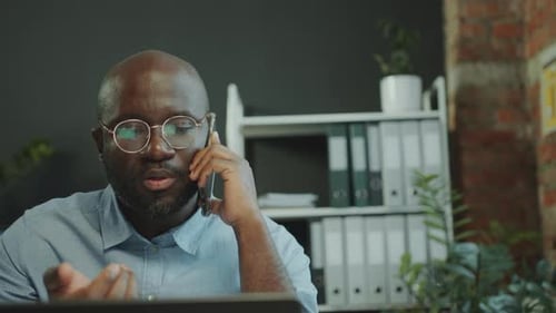 Black Businessman Having Phone Call and Working on Laptop in Office