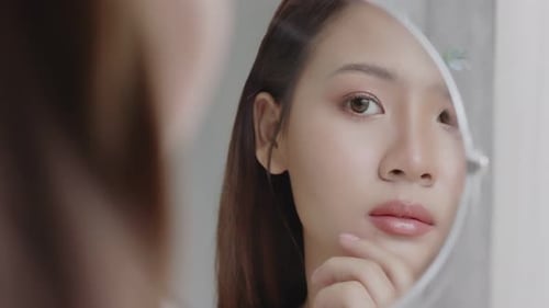Young Asian woman looking at her clean and clear face in the mirror.