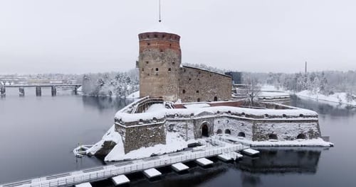Drone flying around the snowy Olavinlinna castle, cloudy winter day in Finland