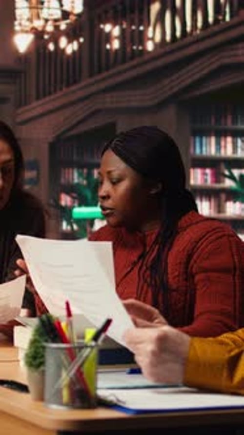 Vidéo verticale : une équipe d'interprètes matures répétant un dialogue scénarisé ensemble dans une bibliothèque