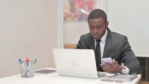 Young Adult Using Phone While Working on Laptop