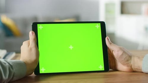 Man Holding and Watching Green Mock-up Screen Digital Tablet Computer While Sitting at the Desk. Ma