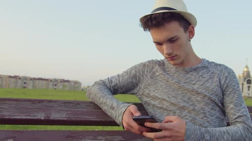 Young Man Using Mobile Phone on Park Bench