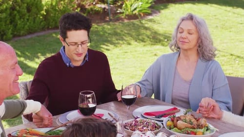 Happy caucasian family praying before dinner in garden